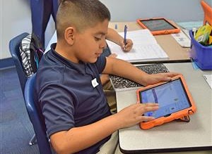 Boy on orange ipad sitting at desk working.